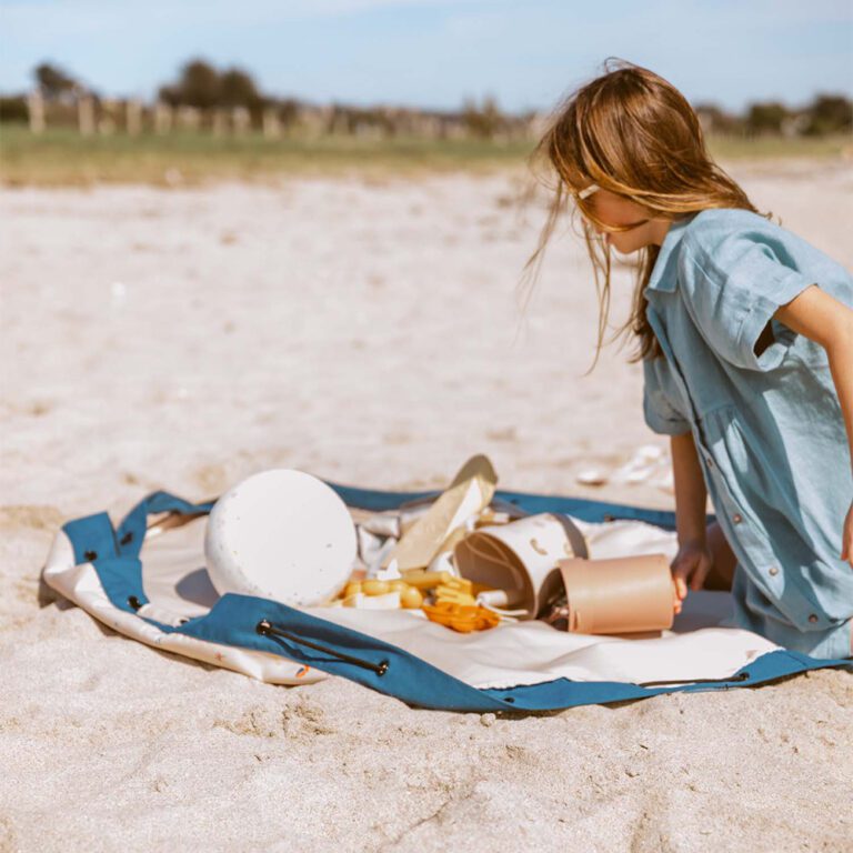 PlayandGo_outdoor_beachbag_magical_days_child_is_looking_at_the_toys_on_the_mat_in_the_sand-768×768
